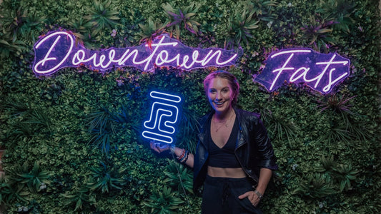 Emily Kenison at Downtown Fats holding a RobeCurls neon sign